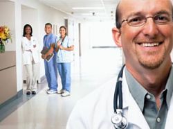 Picture of a male Physician smiling and three Medical Staff (two females and one male) standing in the background behind him smiling as well.